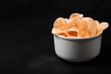 Crispy potato chips in a white plate on a black background. Place for text