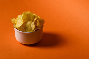 Crispy potato chips in a white cup on an orange background. Place for text