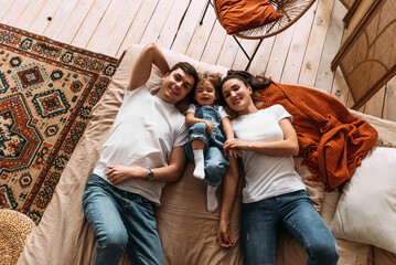 Happy family having fun in the bedroom while they lie on bed. Happy young family. Happy family...