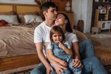 A happy young family spends time together in a home interior. A beautiful happy family spending time together at home. A young married couple with their cute daughter. The family spends time at home