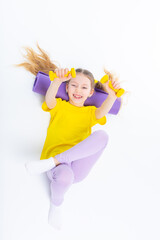 Little cute happy girl lies with dumbbells and gymnastic mat. Isolated on white background. View from above.