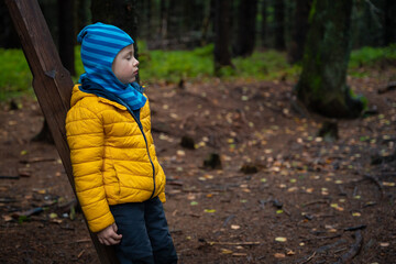 The child rests on the mountain trail, standing, leaning on the post