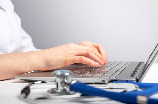 Doctor hands closeup working on laptop. Woman sitting at desk with computer and stethoscope. Patient consultation or search of medicine information. High quality photo