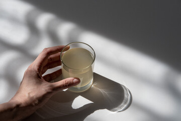 Female hand holding glass of chicken broth. Deep shadows on the table from bright sunlight.
