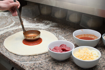 Male chef smears red sauce spicy pizza. Raw dough preform. Production and delivery of pizza