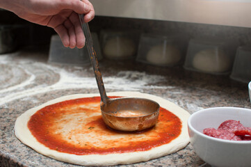 Male chef smears red sauce spicy pizza. Raw dough preform. Production and delivery of pizza