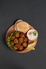 Falafel, cheese balls or meatballs on a wooden tray, with pita and sauce. Top view on a black background