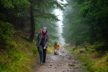 Mum and her little son go on a mountain trail in wet autumn weather. They are accompanied by a dog.