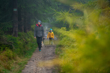 Mum and her little son go on a mountain trail in wet autumn weather. They are accompanied by a dog.