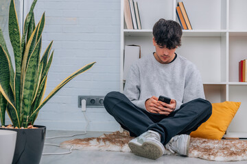 young teenager boy with mobile phone at home sitting comfortably on the floor