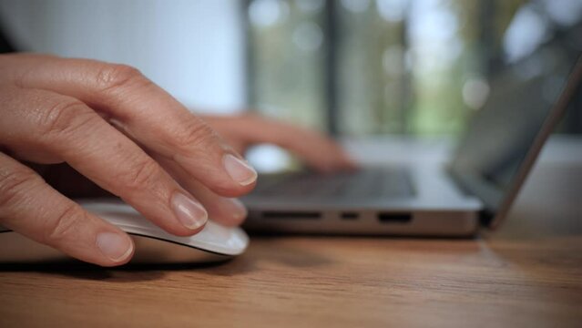 Femme qui travaille sur un ordinateur portable. Gros plan sur la main qui manipule la souris et le clavier. Plan en travelling lent. Vid&eacute;o 4K