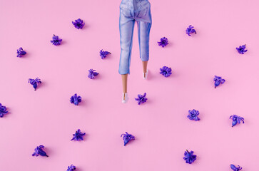 Women's legs in jeans walking in white sneakers on pastel pink background with purple hyacinth flowers. Creative concept for minimal spring background