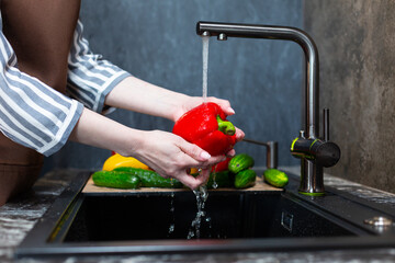Close-up of a woman in an apron in the kitchen washing vegetables before preparing a vegetarian dish.