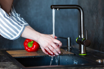 Close-up of a woman in an apron in the kitchen washing vegetables before preparing a vegetarian dish.