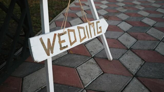 White wooden sign pointer shows the direction of movement. The word inscription wedding on the board. Decor element.