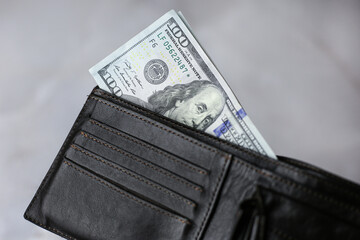 100 dollars banknote in a dark leather wallet on a light background