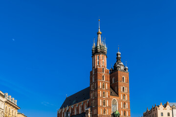 Fototapeta premium St. Mary's Basilica on the main market square of Krakow on a sunny day, the moon and the trail of a jet plane are visible in the blue sky. Tourist travel to European attractions