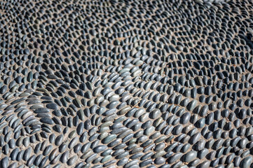 Selective focus on decorative pattern of river rocks laid in garden footpath. 