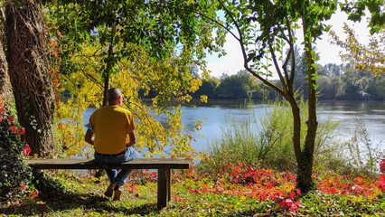 Senior man sitting on a bench near the river in a lush forest