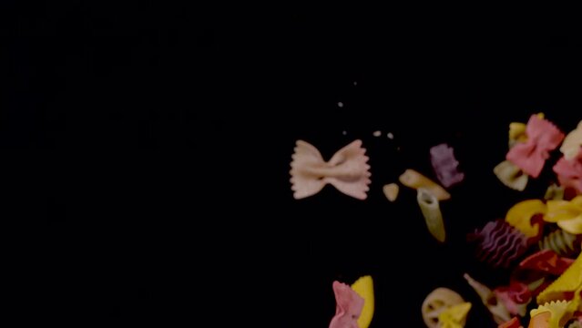 SUPER SLOW MOTION, CLOSE UP, PROBE LENS: Top down view of falling pasta in different shapes and colours. Coloured pasta downfall close up. Detailed view of scattered raw vegetable pasta mix.