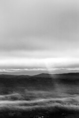 Sun rays coming down from some clouds over a valley filled by fog, illuminating part of it