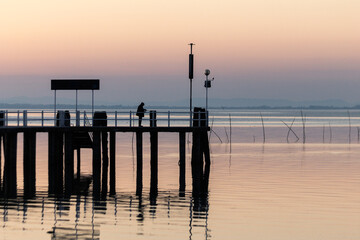 Man fishing on a pier on the lake at sunset