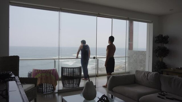 two friends looking at the sea on a terrace of a beach house on a cloudy day in 4k