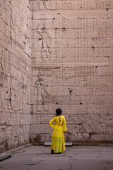 Woman in yellow dress looking at the hieroglyphs of the Temple of Edfu, Egypt