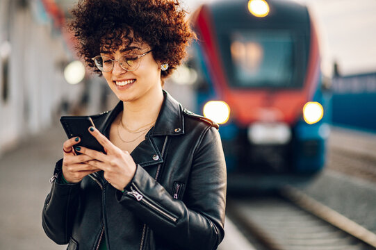 Woman Waiting On A Train Station Platform And Using Smartphone