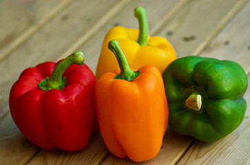 Closeup of four sweet peppers in different colors laying on a wooden table outdoors in summer.