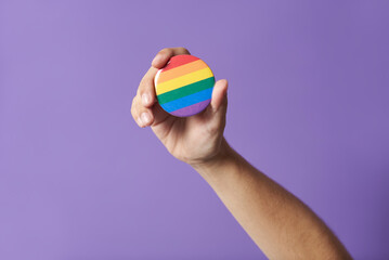 Hand raising a rainbow flag badge, symbol of support for the LGBT community.