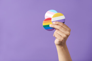 Hand raising three pins with rainbow, trans and non binary flags. LGBT pride. - obrazy, fototapety, plakaty