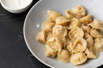 Meat dumplings, homemade russian pelmeni in bowl with sour cream isolated on black background