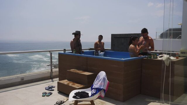 several friends drinking cans of Pilsen beer and wine in the pool on the terrace of a beach house with the sea in the background on a sunny day in 4k - Punta Hermosa, Peru - January 2022