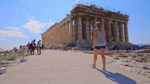 ATHENS, GREECE - JUNE 19, 2021: Rear-view of female walking towards the Parthonon inside the Acropolis on a sunny summer day