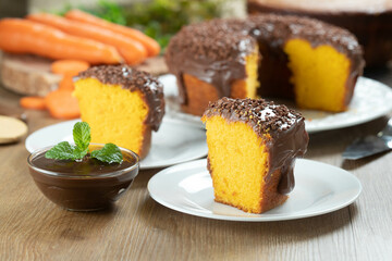 Close up piece of Brazilian carrot cake with chocolate frosting on wooden table with carrots in the background