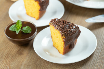 Close up piece of Brazilian carrot cake with chocolate frosting on wooden table with carrots in the background