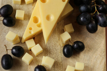 Cheese cut with fruits.Mazdar cheese triangles, gouda cheese cubes and black grapes.Cheese with grapes berries on wooden board background.milk fat and Milk products.