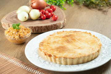 Chicken pie with cottage cheese, tomatoes, onion and olives on wooden table and white plate.