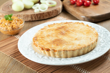 Chicken pie with cottage cheese, tomatoes, onion and olives on wooden table and white plate.