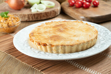 Chicken pie with cottage cheese, tomatoes, onion and olives on wooden table and white plate.