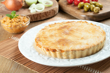 Chicken pie with cottage cheese, tomatoes, onion and olives on wooden table and white plate.