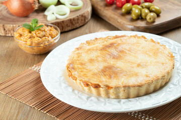 Chicken pie with cottage cheese, tomatoes, onion and olives on wooden table and white plate.