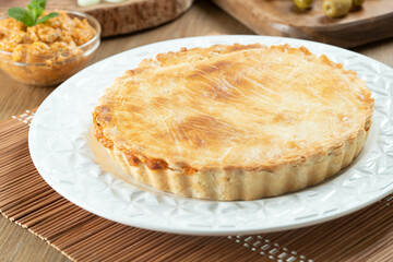 Chicken pie with cottage cheese, tomatoes, onion and olives on wooden table and white plate.