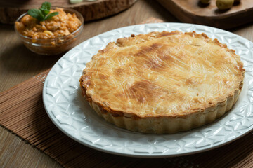 Chicken pie with cottage cheese, tomatoes, onion and olives on wooden table and white plate.