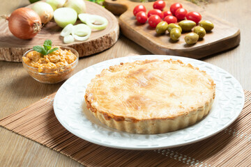 Chicken pie with cottage cheese, tomatoes, onion and olives on wooden table and white plate.