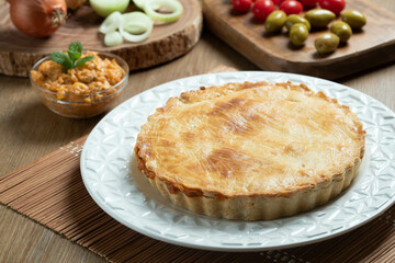 Chicken pie with cottage cheese, tomatoes, onion and olives on wooden table and white plate.