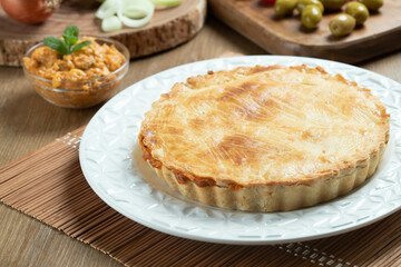 Chicken pie with cottage cheese, tomatoes, onion and olives on wooden table and white plate.
