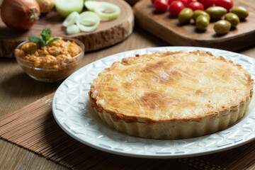 Chicken pie with cottage cheese, tomatoes, onion and olives on wooden table and white plate.