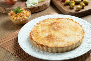 Chicken pie with cottage cheese, tomatoes, onion and olives on wooden table and white plate.